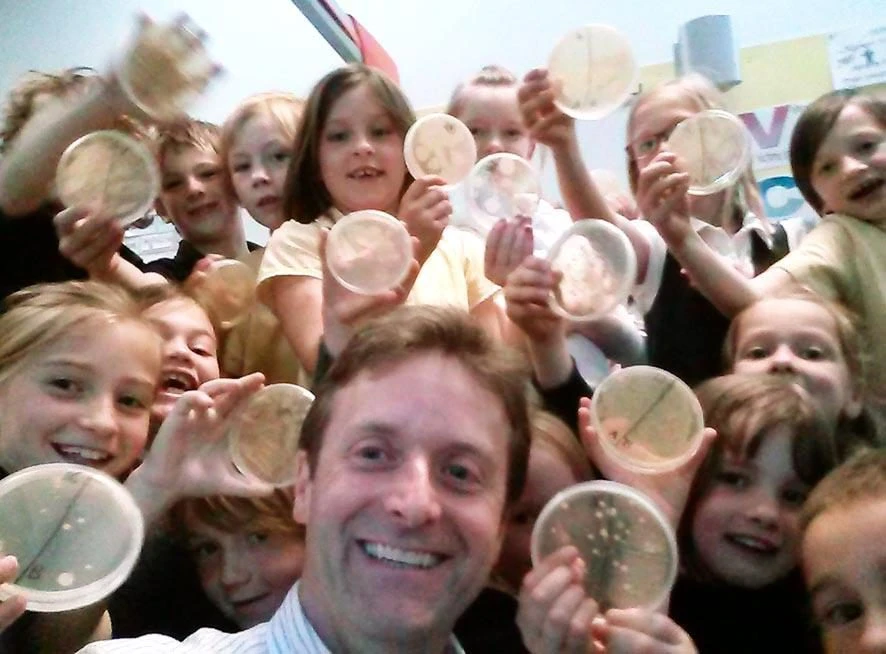 Donald with a group of primary school children holding up agar plates of bacteria